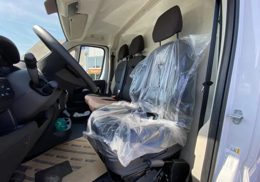 Vue intérieure côté conducteur du Citroën Jumper 2023, sièges avant en tissu avec protection plastique.