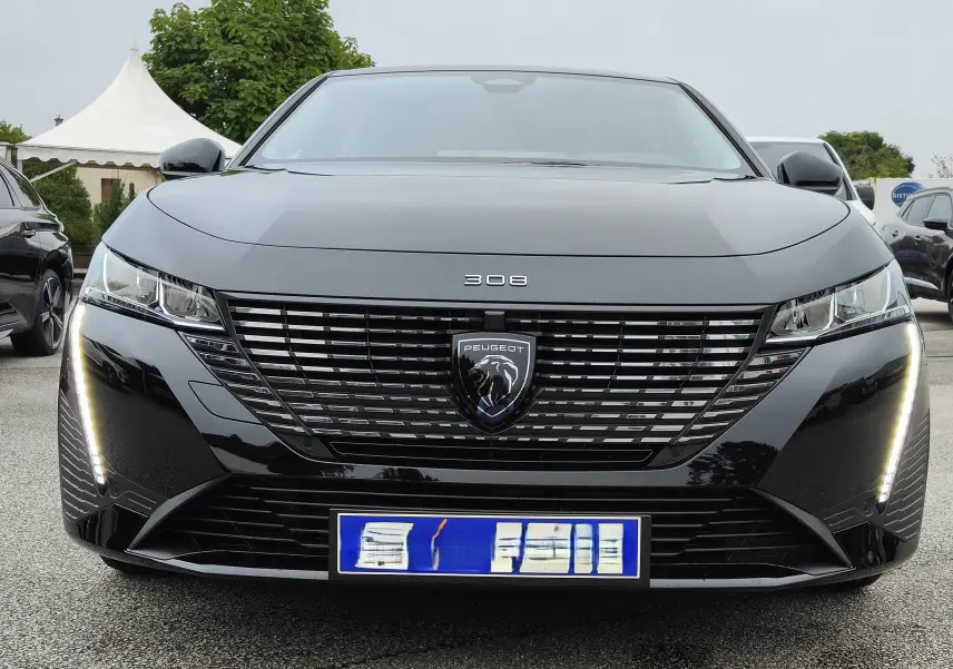 Vue frontale d'une Peugeot 308 PureTech 130 Allure Pack noire de 2023 avec feux LED verticaux allumés.