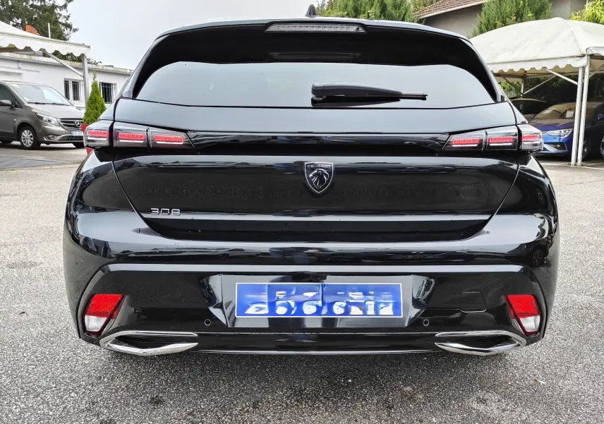 Vue arrière d'une Peugeot 308 PureTech 130 Allure Pack noire de 2023 avec feux LED et double sortie d'échappement chromée.
