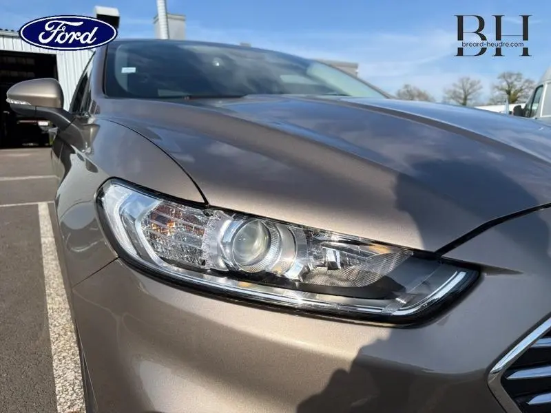 Gros plan sur le phare avant gauche d'une Ford Mondeo 2021 gris Premium Millenium sous un ciel bleu.