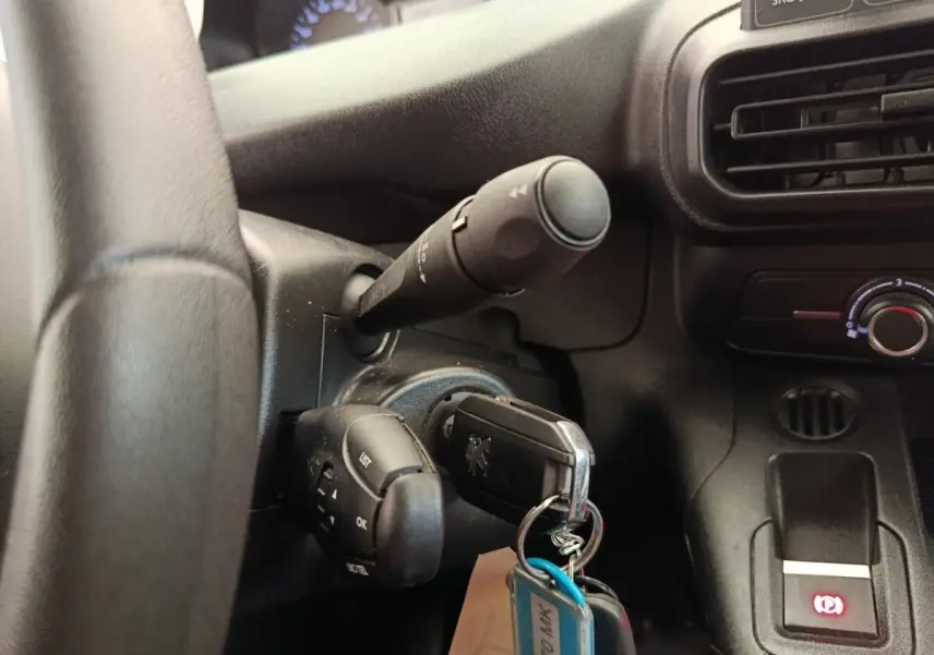 Gros plan sur le volant noir et la clé insérée dans le contact d’un Peugeot Partner blanc, avec commandes au volant visibles.