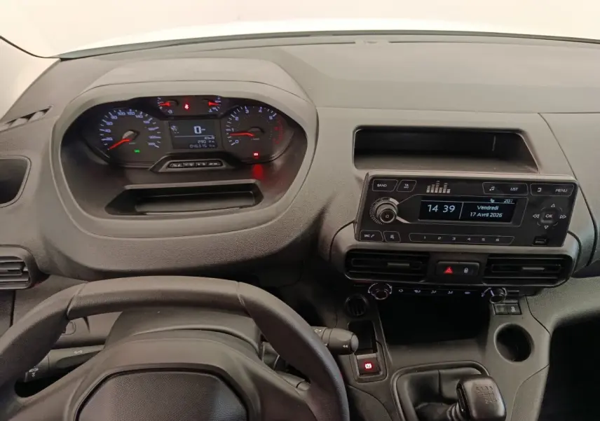 Vue intérieure du tableau de bord et volant noir du Peugeot Partner blanc, avec écran radio et commandes manuelles visibles.