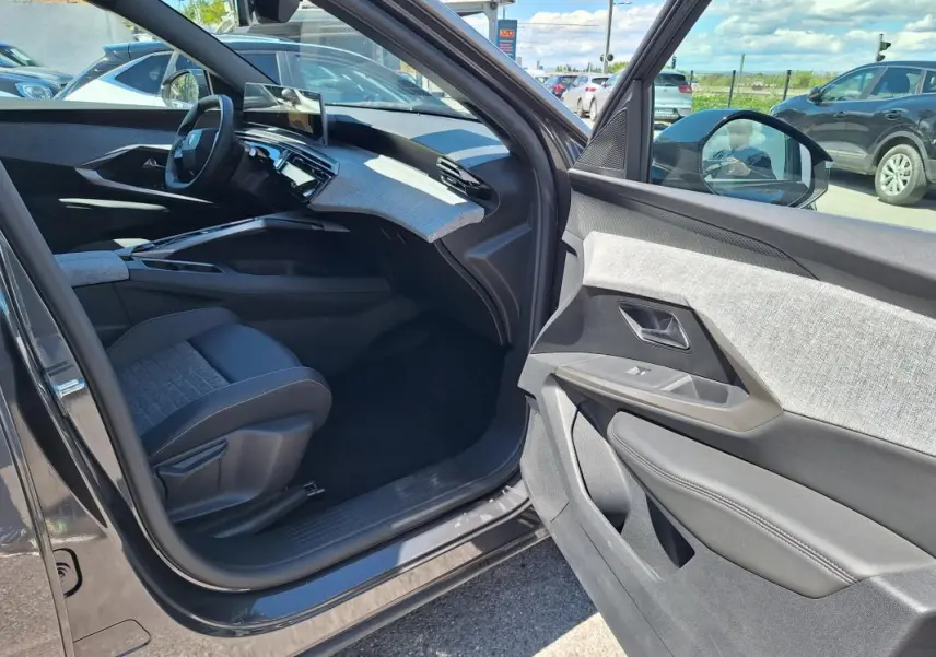 Intérieur côté passager du Peugeot 3008 Hybrid 2025 gris foncé, mettant en valeur la planche de bord et les finitions tissu et cuir.