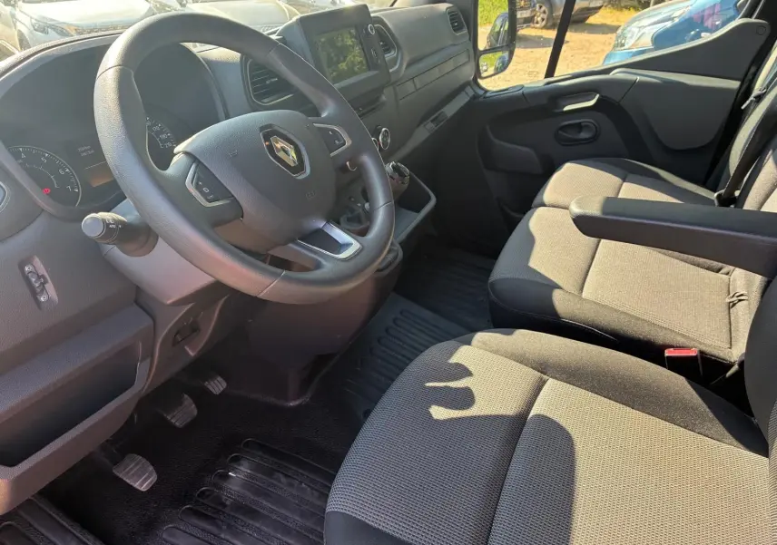 Vue intérieure côté conducteur du Renault Master gris 2023, montrant le volant, la console centrale et les sièges tissu noirs.