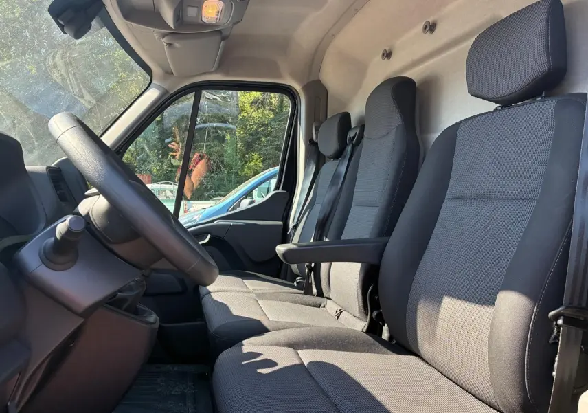 Vue intérieure côté conducteur du Renault Master 2023, sièges tissu gris avec accoudoir et volant visible.