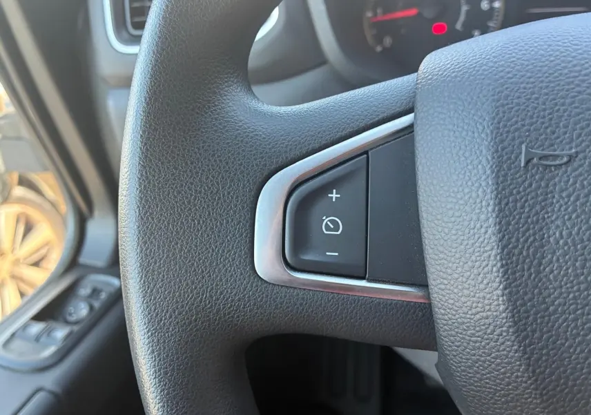 Gros plan sur le bouton de régulateur de vitesse au volant noir du Renault Master gris, vue intérieure côté conducteur.