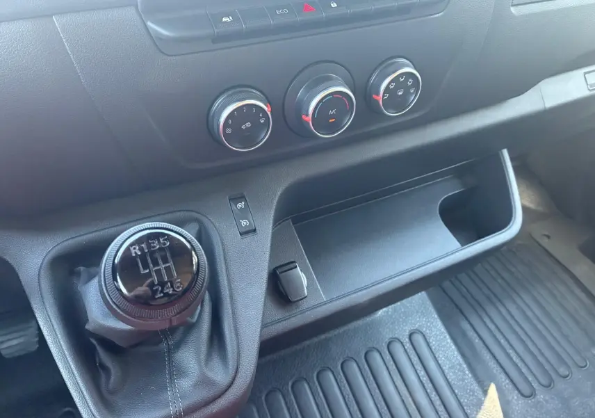 Gros plan sur la console centrale du Renault Master gris 2023, mettant en valeur le levier de vitesses manuel et les commandes de climatisation.