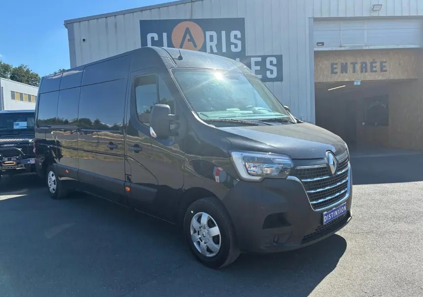 Renault Master gris 3/4 avant droit, grand utilitaire avec calandre chromée et jantes acier, stationné devant un bâtiment.