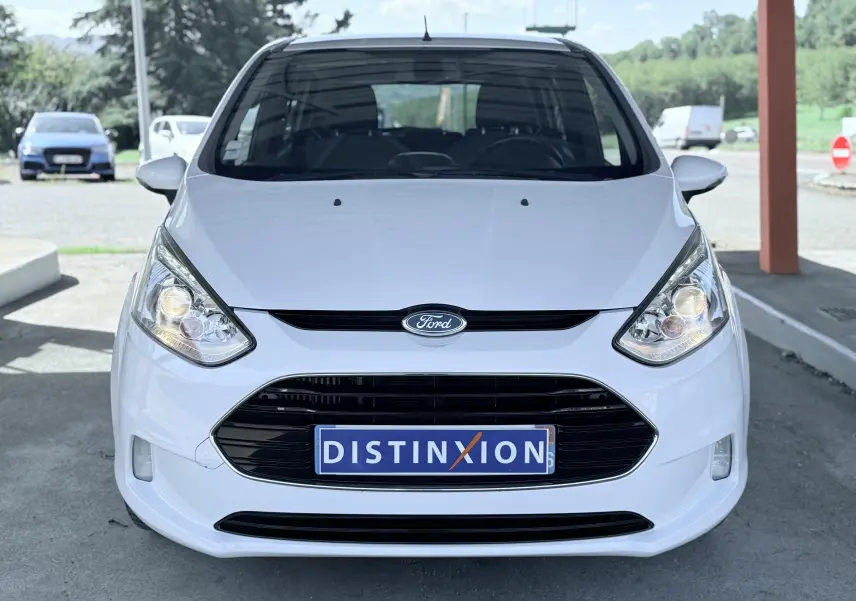 Vue frontale d'une Ford B-MAX blanche 2017 avec calandre noire et phares allumés, plaque Distinxion visible.