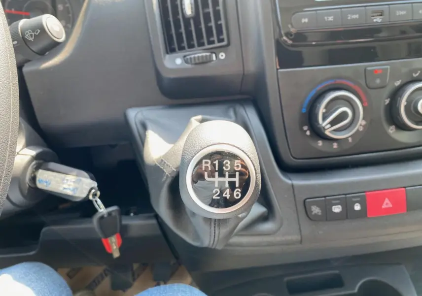 Gros plan sur le levier de vitesses manuel du Peugeot Boxer Fourgon blanc, avec tableau de bord et commandes de climatisation visibles.