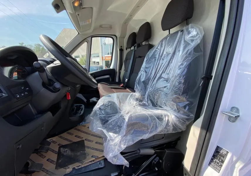 Vue intérieure côté conducteur du Peugeot Boxer Fourgon blanc 2023, sièges avant dont un protégé par un film plastique.