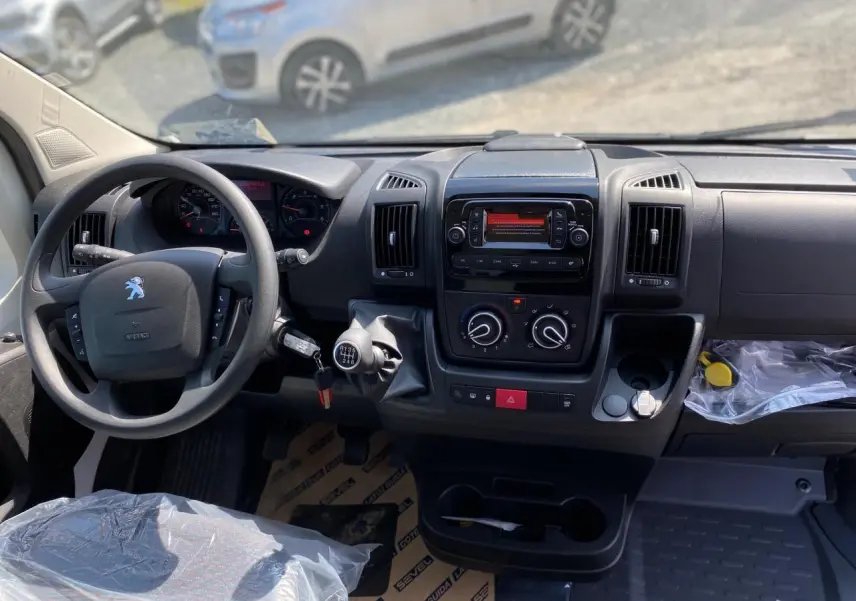 Vue intérieure du tableau de bord du Peugeot Boxer Fourgon blanc 2023, avec volant, levier de vitesse manuel et console centrale.