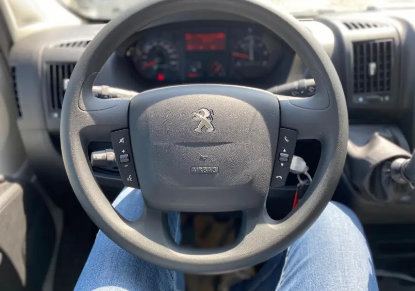 Vue intérieure centrée sur le volant Peugeot du Boxer Fourgon 2023, avec commandes intégrées et tableau de bord flou.