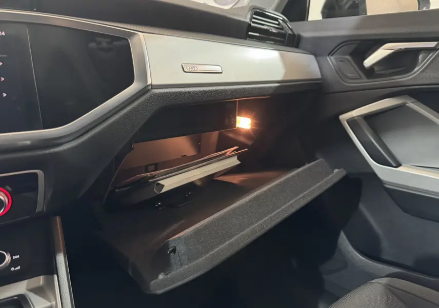 Vue intérieure côté passager de l'Audi Q3 35 TFSI 2022 noire, boîte à gants ouverte avec lumière intérieure allumée.