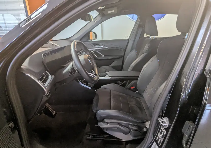 Intérieur noir côté conducteur du BMW X1 2025, sièges M Alcantara, volant cuir M et tableau de bord luxe visible.