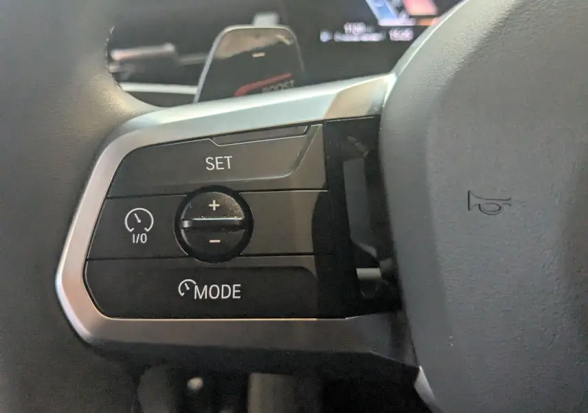 Gros plan sur les commandes de régulateur de vitesse au volant cuir M du BMW X1 noir, côté gauche.