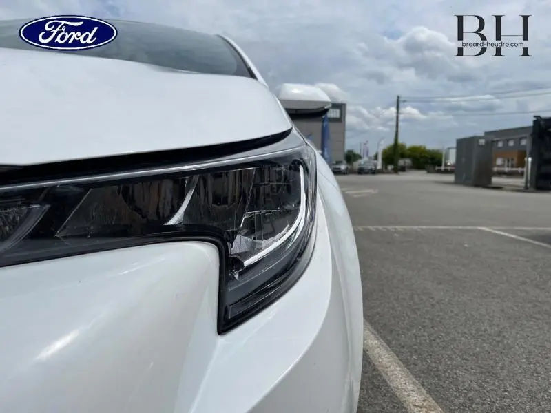 Gros plan sur le phare avant droit d'une voiture blanche, avec un design moderne et des lignes anguleuses.