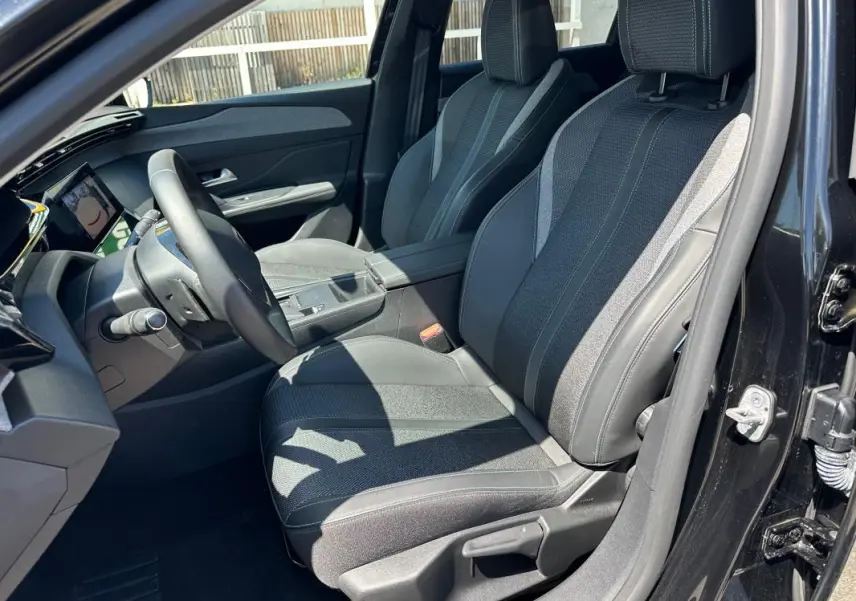 Vue intérieure côté conducteur de la Peugeot 308 SW Hybrid noire, mettant en valeur les sièges en tissu et cuir avec accoudoir central.