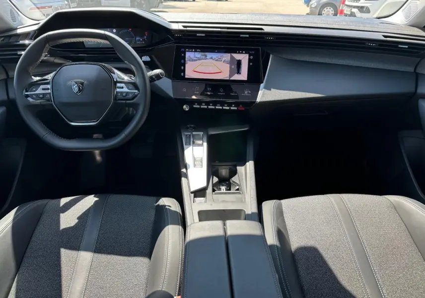 Intérieur noir de la Peugeot 308 SW Hybrid 2025, vue de face sur le volant, écran tactile et console centrale moderne.