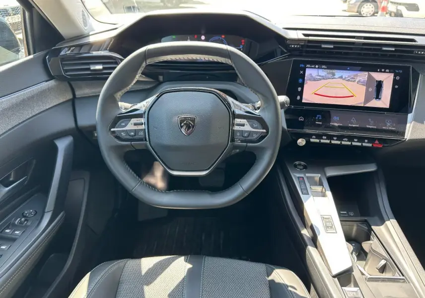 Vue intérieure frontale du poste de conduite noir du Peugeot 308 SW Hybrid avec volant multifonction et écran tactile de caméra de recul.
