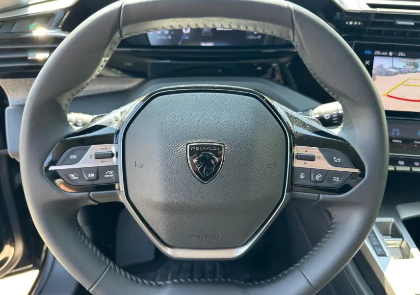 Vue rapprochée du volant noir de la Peugeot 308 SW Hybrid 145 e-DCS6 Allure avec commandes intégrées et logo central.