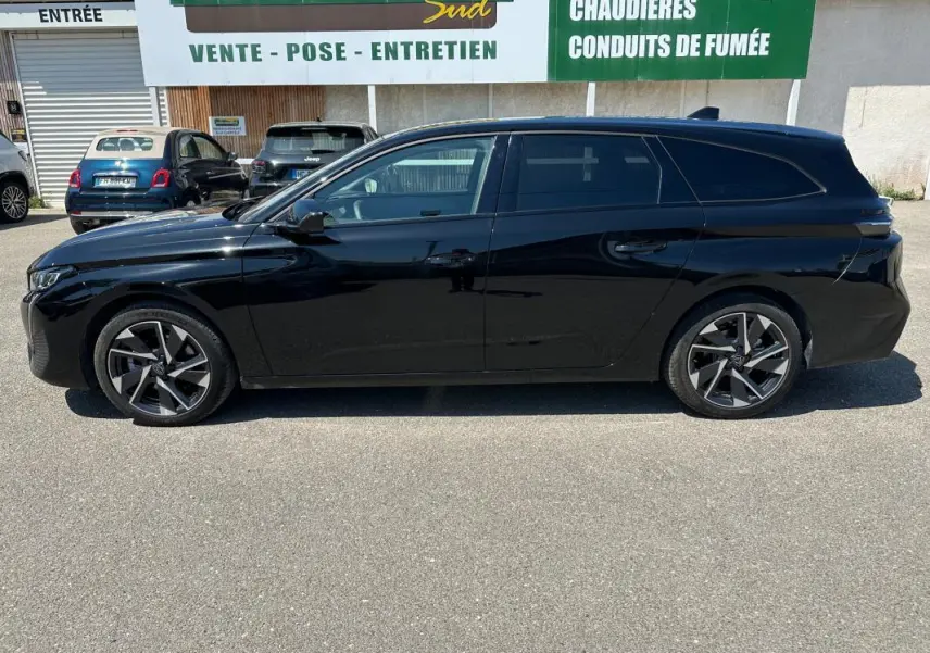 Profil latéral gauche d'une Peugeot 308 SW Hybrid noire 2025 avec jantes alliage 17 pouces, stationnée en extérieur.