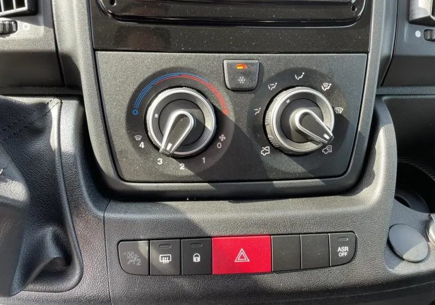 Gros plan sur les commandes de climatisation et les boutons de sécurité du tableau de bord noir du Peugeot Boxer Fourgon blanc.