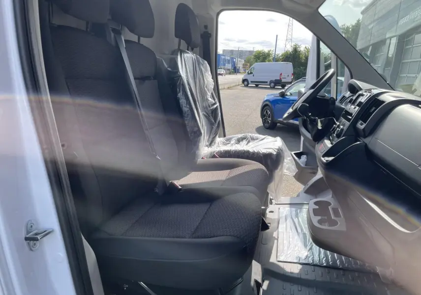 Intérieur du Peugeot Boxer Fourgon blanc 2023 vu côté conducteur, sièges noirs et tableau de bord avec porte-gobelets.