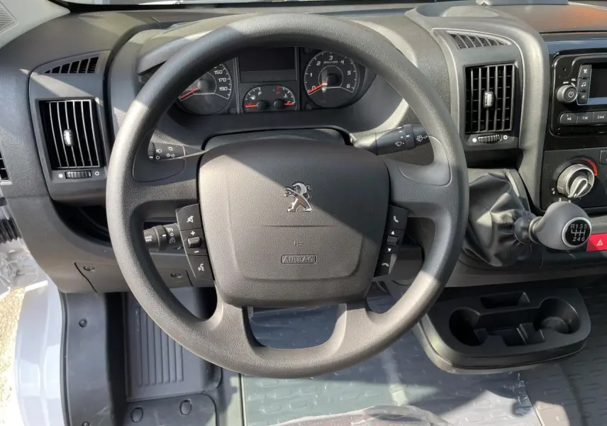 Vue rapprochée du volant noir et tableau de bord du Peugeot Boxer Fourgon blanc, avec levier de vitesses manuel visible.