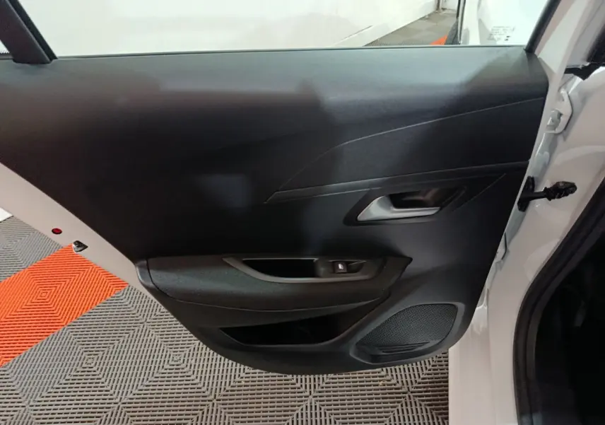 Vue intérieure de la porte avant droite noire d'une Peugeot 208 électrique blanche 2023, avec poignée et haut-parleur intégrés.