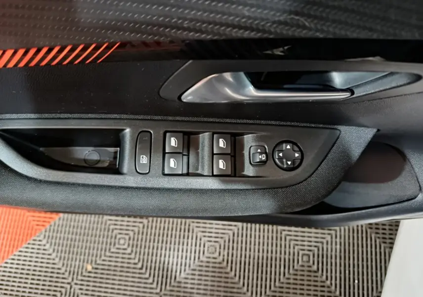 Gros plan sur la commande des vitres et rétroviseurs côté conducteur de la Peugeot 208 électrique blanche.