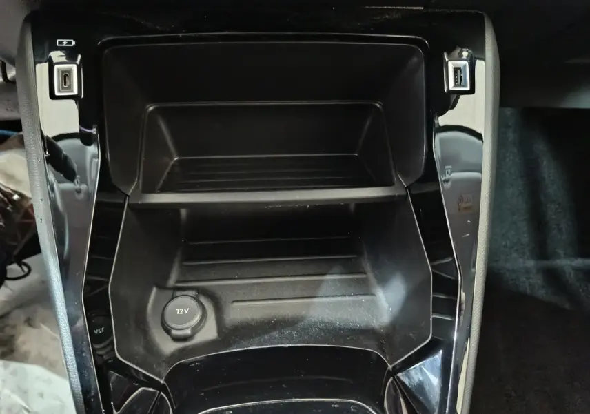Vue rapprochée de la console centrale noire du Peugeot 208 électrique 2023 avec prises USB et prise 12V visible.