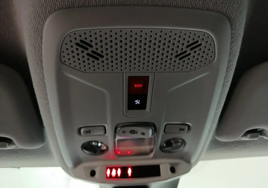 Vue en gros plan du panneau de commandes au plafond avec bouton SOS rouge dans l'habitacle de la Peugeot 208 électrique blanche 2023.