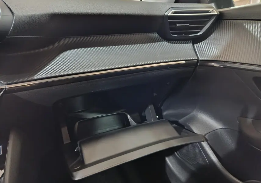 Vue intérieure côté passager de la Peugeot 208 électrique 2023, tableau de bord avec finition carbone et boîte à gants ouverte.