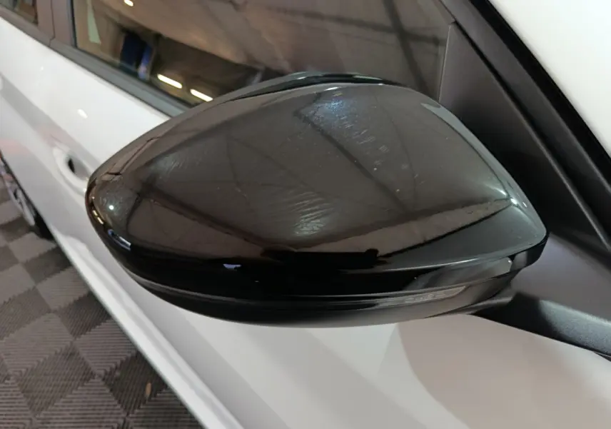 Rétroviseur noir côté gauche d'une Peugeot 208 électrique blanche vue de près en intérieur.