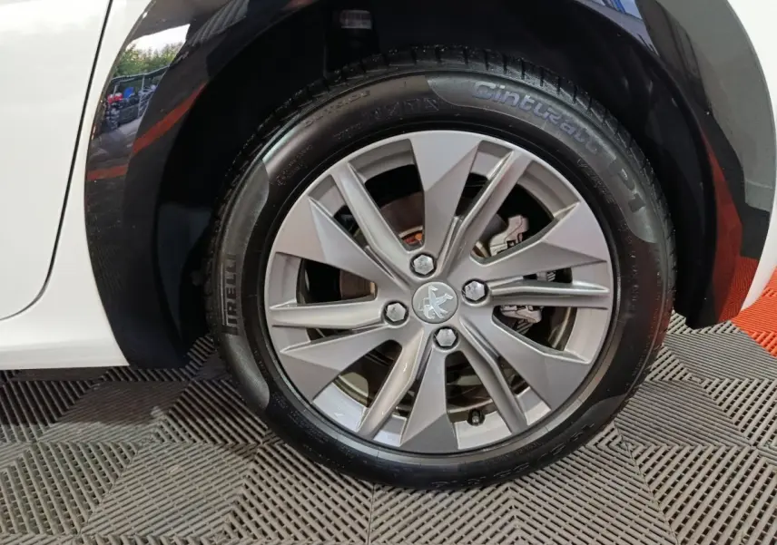 Gros plan sur la roue avant gauche blanche d'une Peugeot 208 électrique 2023 avec jante argentée et logo lion central.