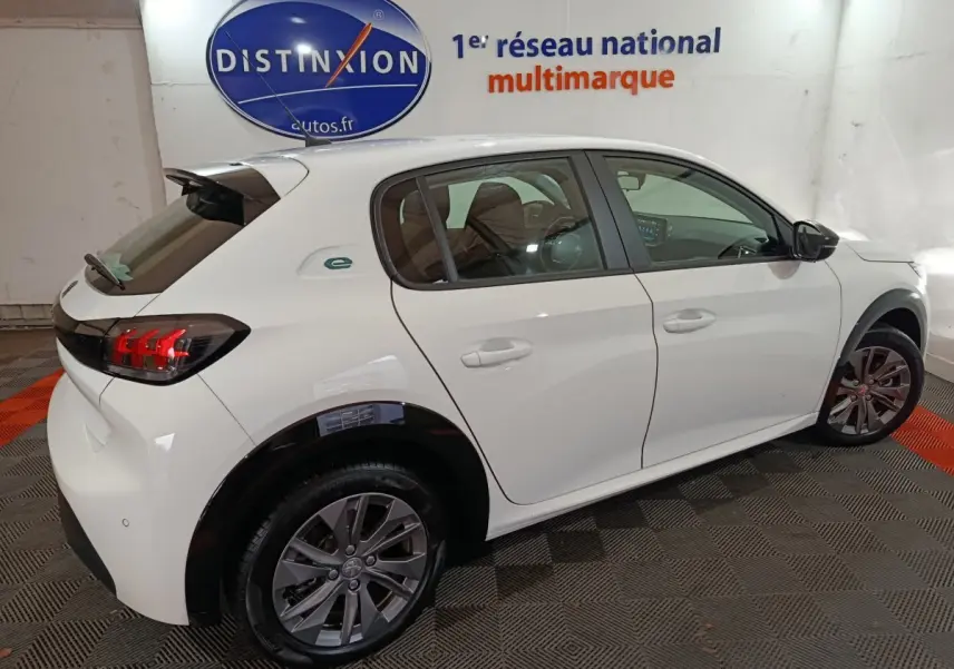 Vue 3/4 arrière droite d'une Peugeot 208 électrique blanche 2023 avec jantes alliage et logo e- sur l'aile arrière.