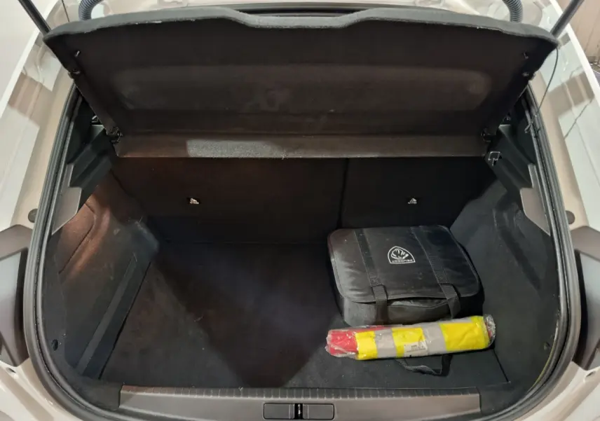 Coffre ouvert vu de dessus d'une Peugeot 208 électrique blanche avec sac de secours et triangle de signalisation.