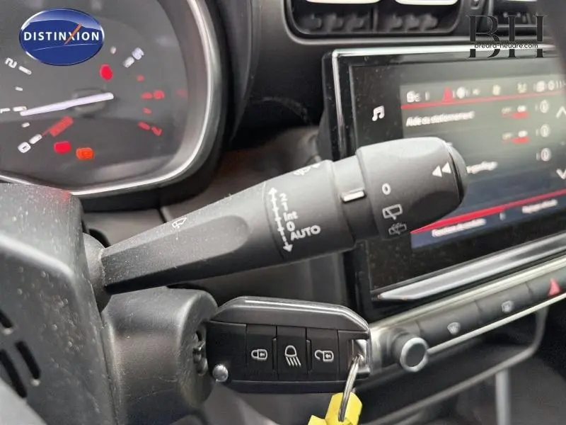 Gros plan sur la commande d'essuie-glace et le tableau de bord noir d'une Citroën C3 Aircross blanche, avec clé insérée.