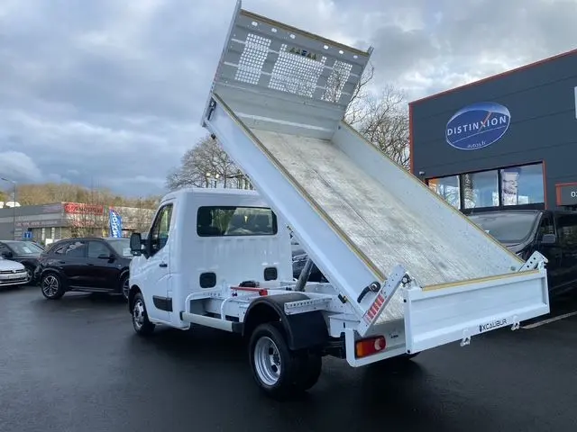 Vue 3/4 arrière droite d’un Renault Master blanc 2024 avec benne basculante relevée sur parking.