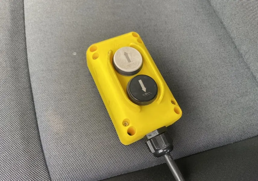 Gros plan sur une télécommande jaune avec deux boutons fléchés, posée sur un siège en tissu gris du Renault Master blanc.