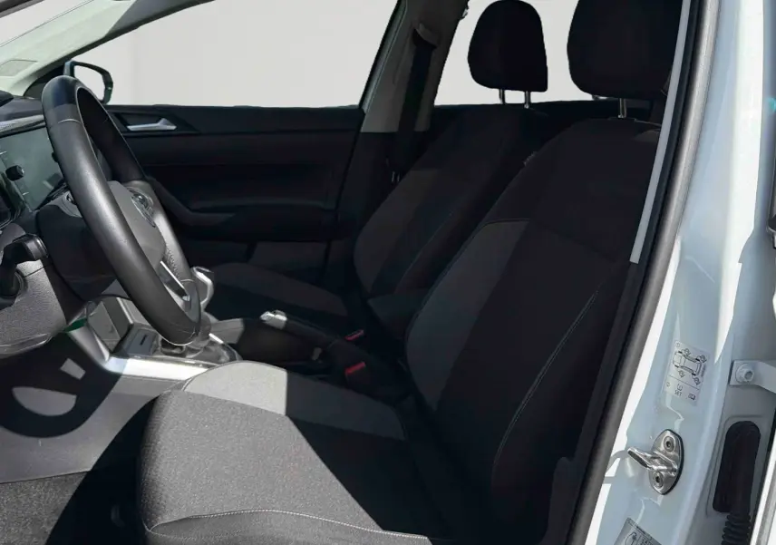 Intérieur avant côté conducteur d'une Volkswagen Polo blanche 2025, sièges noirs et volant cuir multifonctions visible.