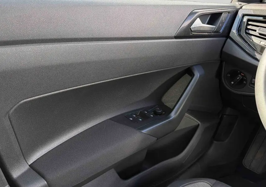 Détail de la porte avant gauche noire de la Volkswagen Polo 2025 avec commandes électriques des vitres et poignée intégrée.