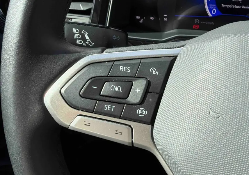 Gros plan sur les commandes du régulateur de vitesse au volant cuir gris d’une Volkswagen Polo blanche 2025.