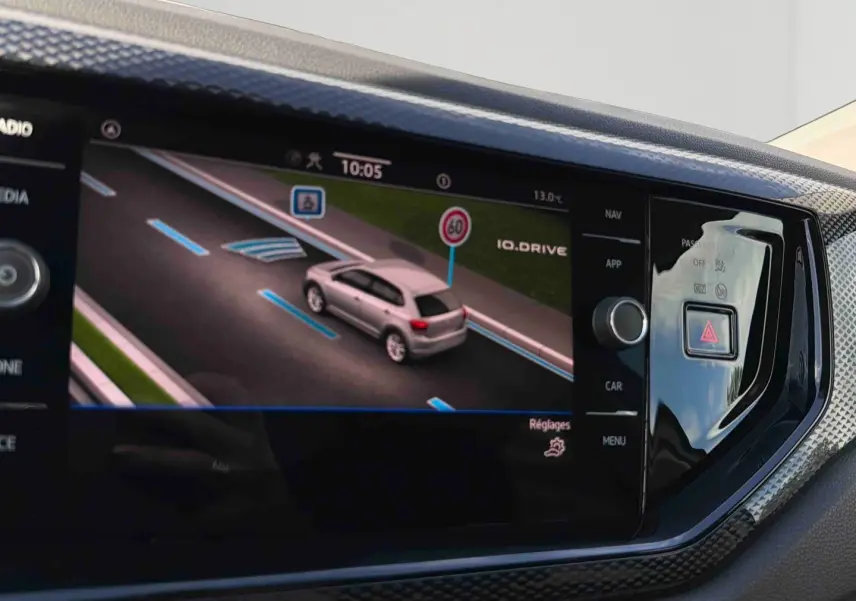 Écran tactile intérieur montrant la simulation d’une Volkswagen Polo blanche en conduite assistée sur route.