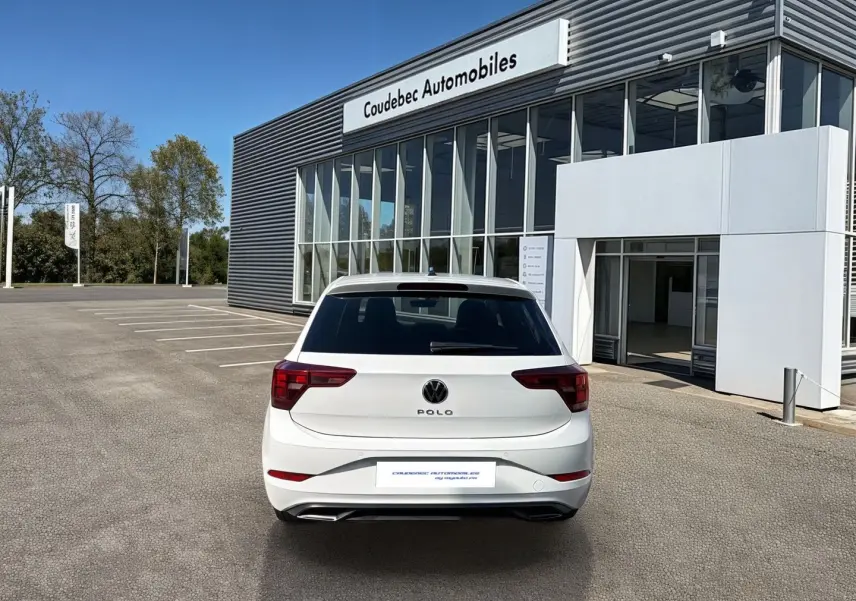 Vue arrière d'une Volkswagen Polo blanche 2025 stationnée devant un bâtiment moderne de concession automobile.