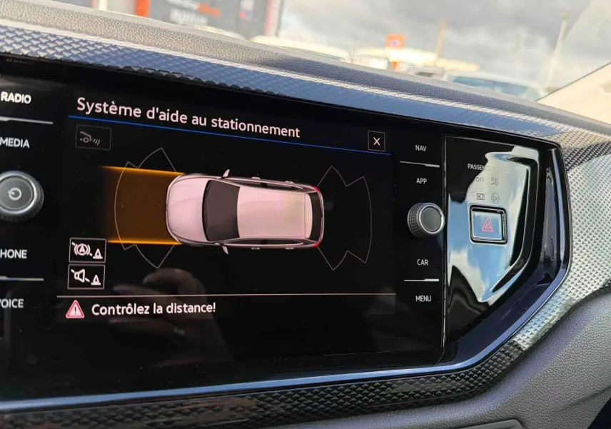 Écran tactile intérieur montrant le système d'aide au stationnement de la Volkswagen Polo blanche, vue de face.