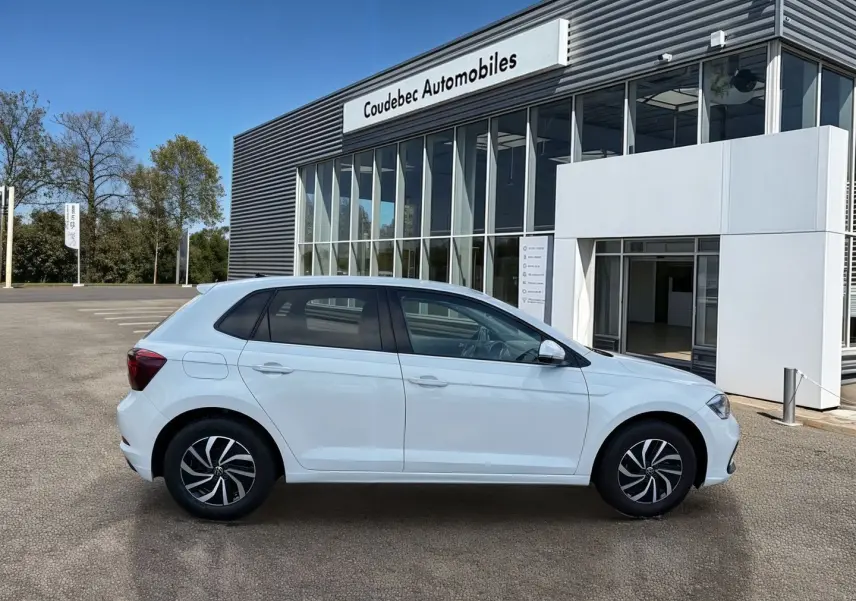 Volkswagen Polo blanche vue de profil côté gauche, garée devant un bâtiment moderne de concession.