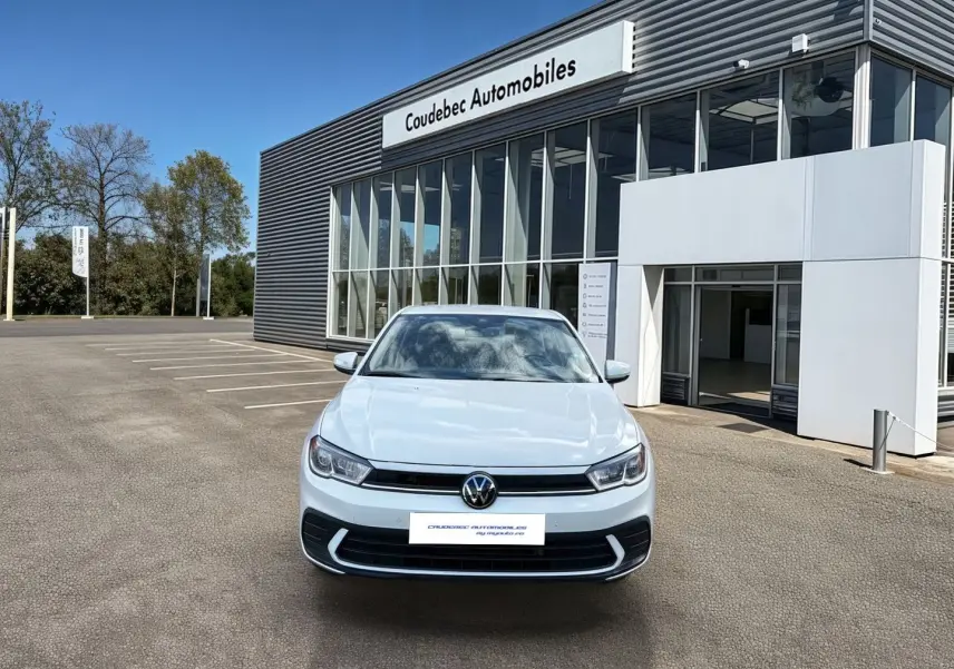 Volkswagen Polo blanche vue de face, avec calandre noire et feux LED, devant un bâtiment de concession automobile.
