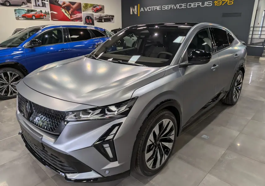 Renault Rafale E-Tech gris schiste satin en 3/4 avant droit, avec calandre noire et jantes bicolores distinctives.